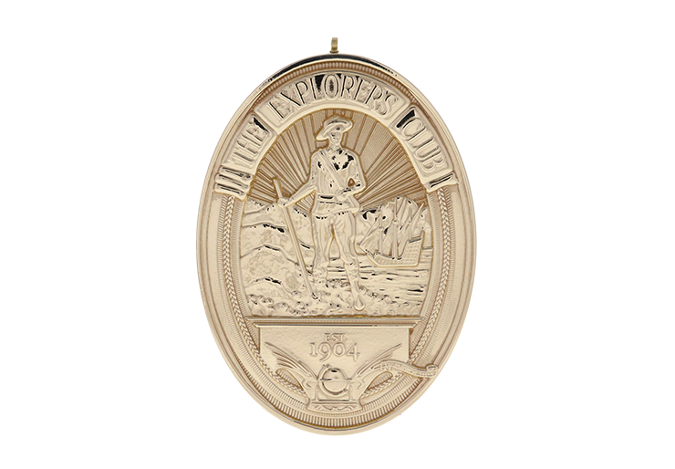 The Explorers Club gold oval medallion with a detailed textured image
